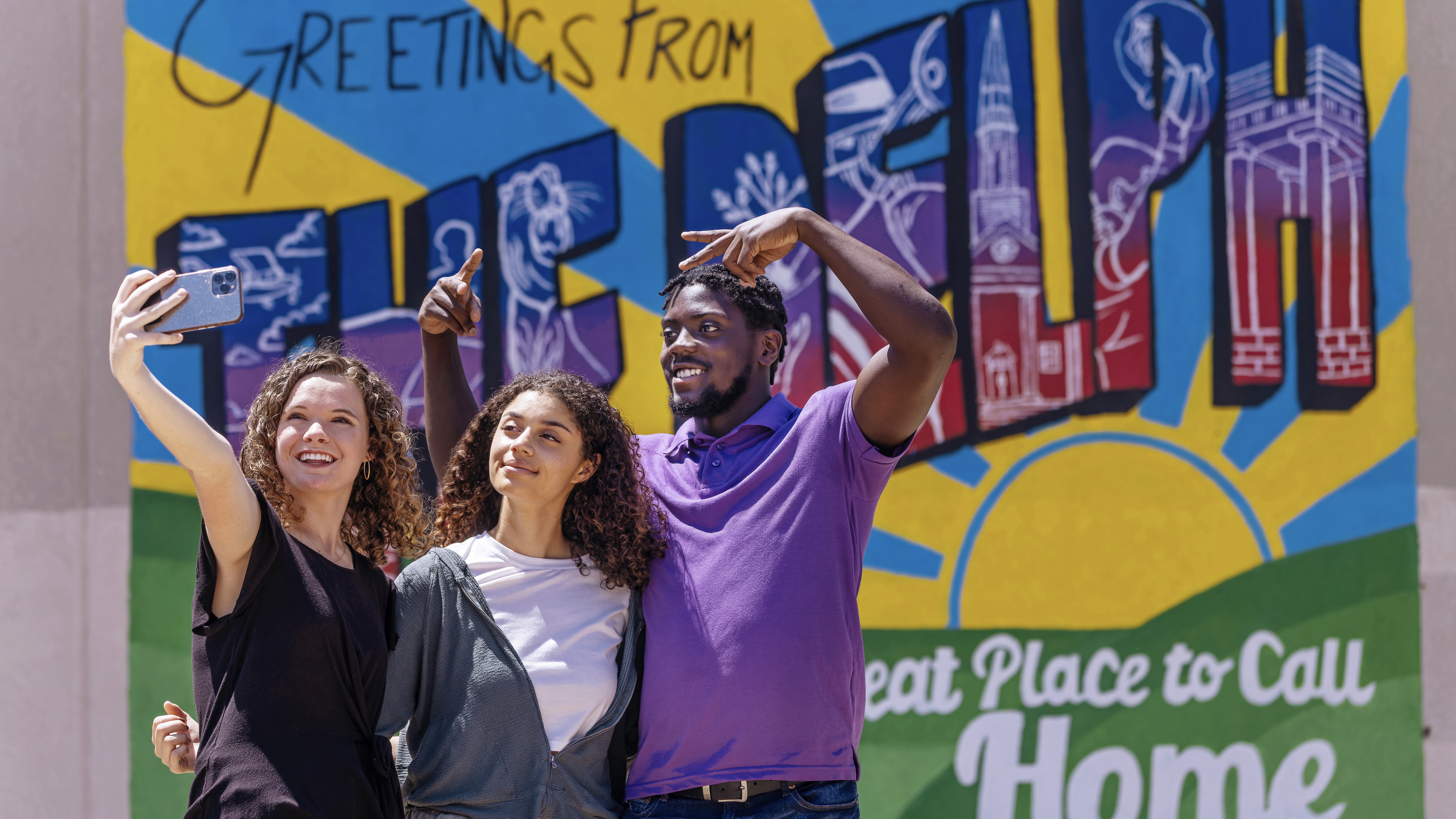 Students take photographs in front of a mural in downtown Arkadelphia